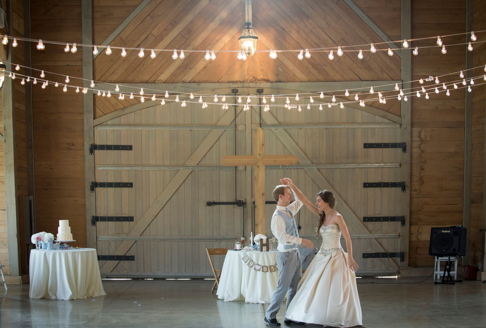 A couple dancing in front of big barn doors under strings of lights