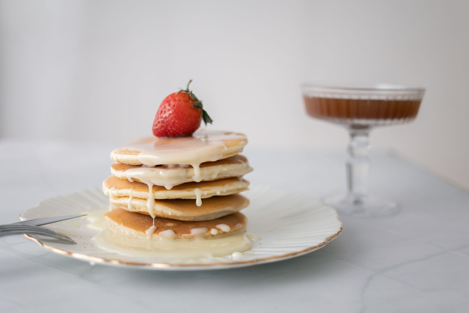 A tall stack of pancakes with a strawberry on top on a white plate