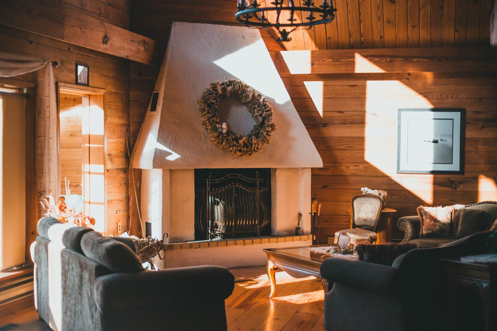 A wood-paneled living room with a white stucco fireplace, a wreath above it and deep armchairs