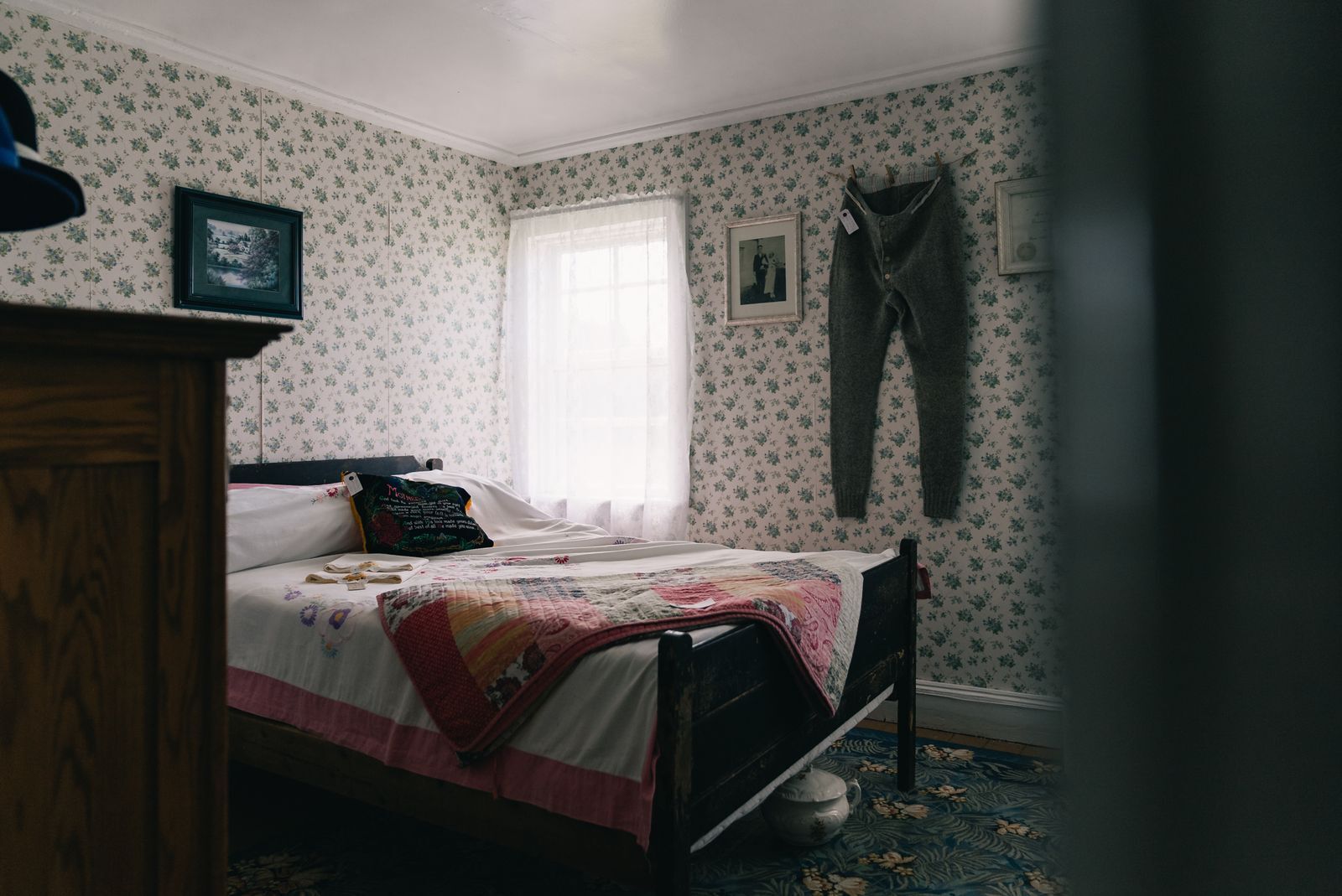 A guest room with floral wallpaper, a dark wooden bed made up with a patchwork quilt, and a window